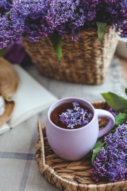 Bir fincan çay, hasır şapka ve leylak sepeti, bahar durgun hayat.