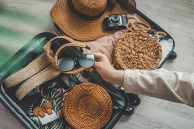 Ahşap masada güneş gözlüğü, şapka, çanta ve diğer şeyleri tutan bir kadın. Seyahat kavramı.