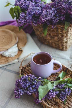 Bir fincan çay, hasır şapka ve leylak sepeti, bahar durgun hayat.