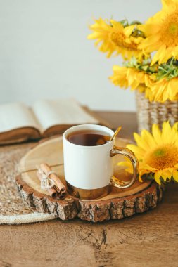 A cup of tea with cinnamon on a wooden tray and an open vintage book with sunflowers, aesthetics