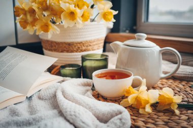 Bir fincan çay, mumlar, açık kitap nergisli sepet, bahar estetik fotoğrafı..
