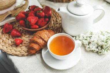 Bir fincan çay, kruvasan, çilek ve leylak sepeti, yaz sabahı estetiği..