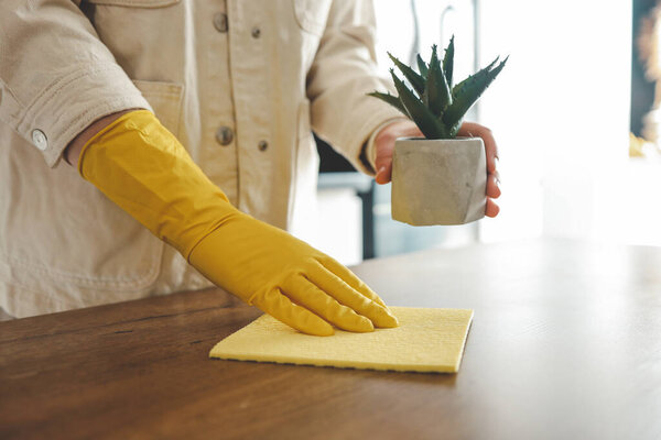 Closeup on woman's hands in yellow protective rubber gloves cleaning kitchen cabinets with sponge.