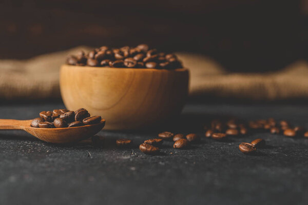 Coffee beans in a wooden plate on a black background.
