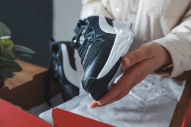 Unpacking women's shoes, stylish white sneakers in hands.