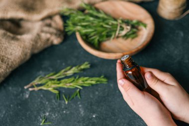 Esans taze biberiye dallar üzerinde karanlık bir arka plan ile bir şişe.