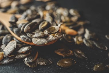 Siyah bir arka planda tahta bir kaşığa kabak tohumları serpiştirmek.