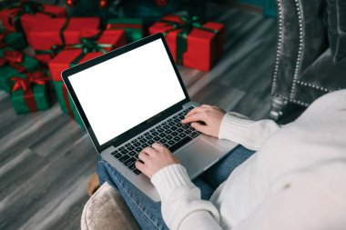 Genç bir kadın dizüstü bilgisayarda çalışıyor. Boş ekran ve taklit alanı var. Modern ev oturma odası iç tasarımı. Noel, Yeni Yıl dekore edilmiş çalışma alanı.