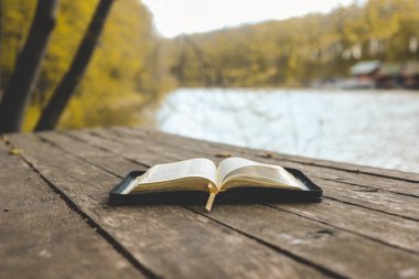 Open Bible on a wooden board near the river.