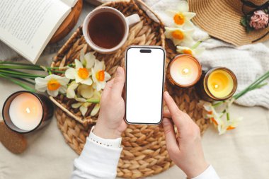 İzole edilmiş ekranlı telefon ve mum ve çiçeklerden oluşan bahar kompozisyonu.