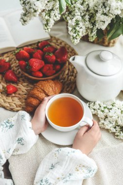 Ellerinde çay, çilek ve çiçekler, yaz kahvaltısı konsepti..