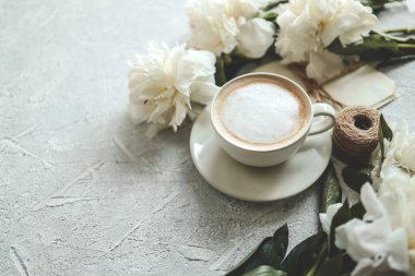 Yaz kompozisyonu üst görünümü. Bir fincan kahve, şakayık ve gri arka planda klasik mektuplar..