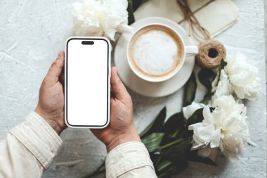 Bir fincan kahvenin arka planında izole bir ekran olan telefon elinde..