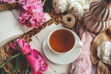 Güzel bahar kompozisyonu, günaydın konsepti. Bir fincan çay, şakayık ve açık bir kitap..