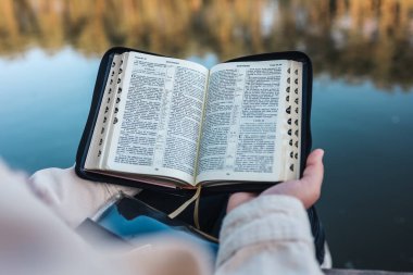 Girl reading the Bible on the river bank.