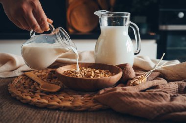 Süt sürahisi, işlenmemiş tam tahılların karışımından yapılmış doğal müsli ile kaseye süt döküyor..