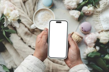 Bir fincan kahvenin arka planında izole bir ekran olan telefon elinde..