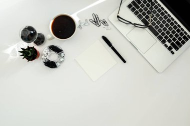 Boş defter, bilgisayar klavyesi ve diğer ofis malzemeleriyle dolu beyaz ofis masası. Kopyalama alanı olan üst görünüm, düz yatay.