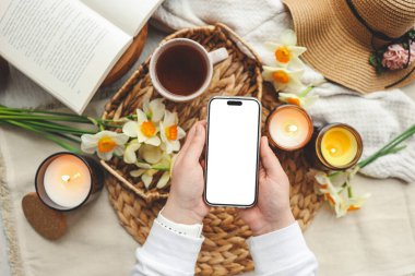 İzole edilmiş ekranlı telefon ve mum ve çiçeklerden oluşan bahar kompozisyonu.