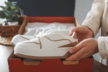 Unpacking women's shoes, stylish white sneakers in hands.