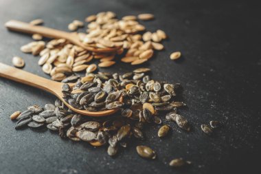 Siyah bir arka planda tahta bir kaşığa kabak tohumları serpiştirmek.