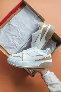 Unpacking women's shoes, stylish white sneakers in hands.