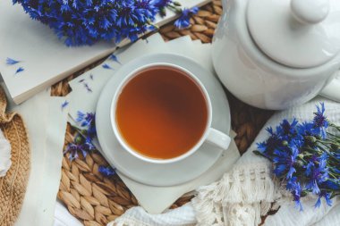 Bir fincan çay, açık kitap ve çiçek, üst manzara..