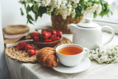Bir fincan çay, kruvasan, çilek ve leylak sepeti, yaz sabahı estetiği..