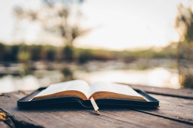 Open Bible on a wooden board near the river.