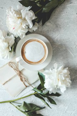 Yaz kompozisyonu üst görünümü. Bir fincan kahve, şakayık ve gri arka planda klasik mektuplar..