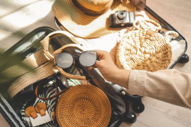 Ahşap masada güneş gözlüğü, şapka, çanta ve diğer şeyleri tutan bir kadın. Seyahat kavramı.