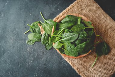 Ahşap bir kâse içinde taze organik ıspanak yaprakları koyu kırsal arka planda. Kopyalama alanı olan üst görünüm.