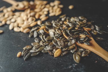 Siyah bir arka planda tahta bir kaşığa kabak tohumları serpiştirmek.