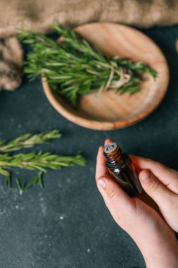 Esans taze biberiye dallar üzerinde karanlık bir arka plan ile bir şişe.