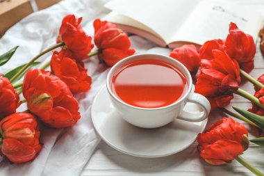 Güzel bahar kompozisyonu, günaydın konsepti. Bir fincan çay, şakayık, açık kitap..