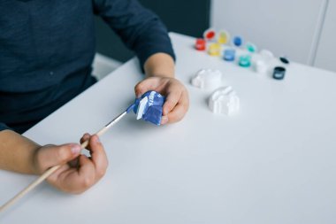 Çocuk alçı figürünü parlak renklerle boyuyor. Çocukların yaratıcılığı kavramı. Anaokulu öğrencisi evde dikiş işi yapıyor..