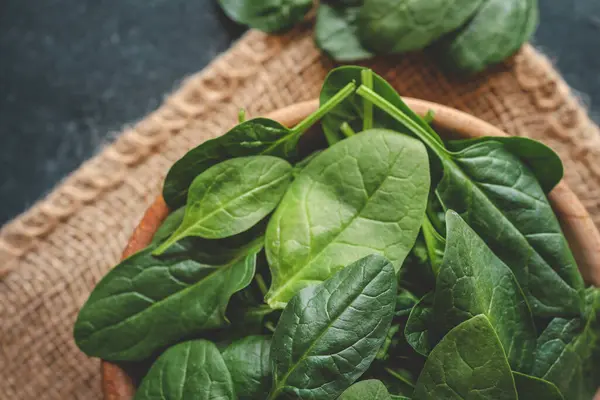 Ahşap bir kâse içinde taze organik ıspanak yaprakları koyu kırsal arka planda. Kopyalama alanı olan üst görünüm.