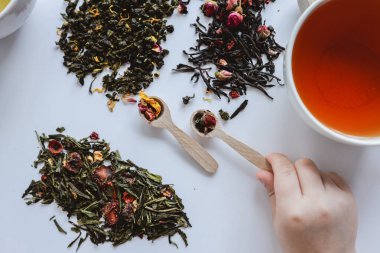 Beyaz bir arka planda elinde yaprak çayıyla kaşık çay zamanı..