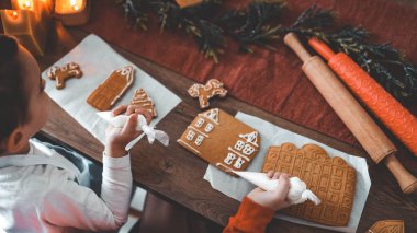 Çocuklar zencefilli kurabiye evi dekore eder, sade Noel atmosferi.