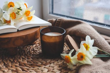 Pencerenin kenarında mum ve nergis, bahar kompozisyonu.