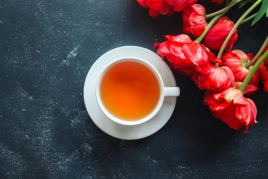 Bir fincan çay ve kırmızı şakayıklar koyu arkaplanda üst görünüm, metin için boşluk.