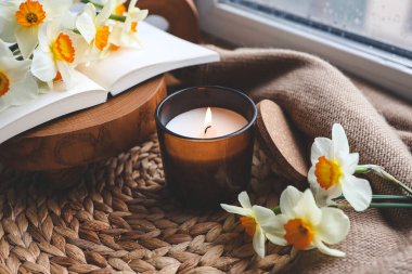 Pencerenin kenarında mum ve nergis, bahar kompozisyonu.