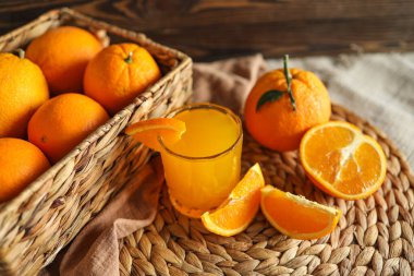 Bir bardak portakal suyu, dilimlenmiş portakal ve bir sepet portakal. Portakallar parlak ve taze..