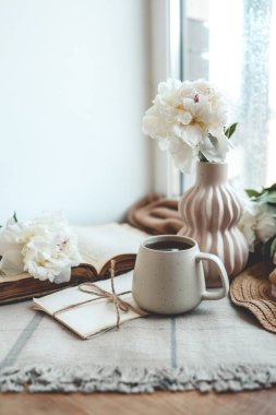 Bir fincan çay, hasır şapka, açık kitap ve şakayıklar, bahar durgun hayat..