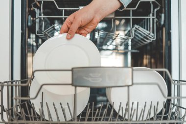 Kadın el doldurma, boşaltma ya da bulaşık makinesini çatal bıçak ile boşaltma. Mutfak aletleri, yaşam tarzı manzarası. Kadın bulaşık makinesine bir tabak koyar ya da ondan alır. Ev hanımı ev işlerini yapar..