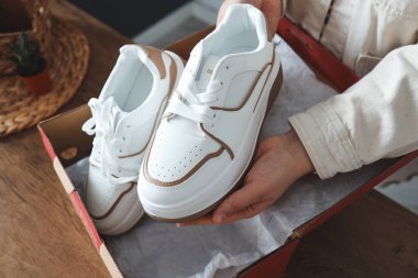 Unpacking women's shoes, stylish white sneakers in hands.