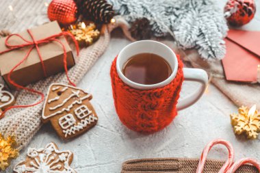 Kırmızı süslemeli bir fincan çay, zencefilli çörek, şeker, mum ve çelenk. Evde Noel atmosferi.