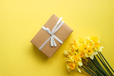 Bir buket nergis ve renkli arka planda bir hediye kutusu, yazı için yeri olan üst manzara. Taze bahar çiçekleri.