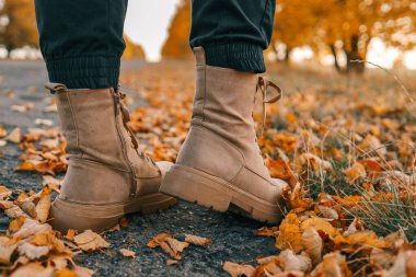 Bir adam sonbahar yolu boyunca yürüyor, botları yakın çekimde..