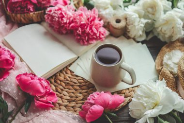 Güzel bahar kompozisyonu, günaydın konsepti. Bir fincan çay, şakayık ve açık bir kitap..